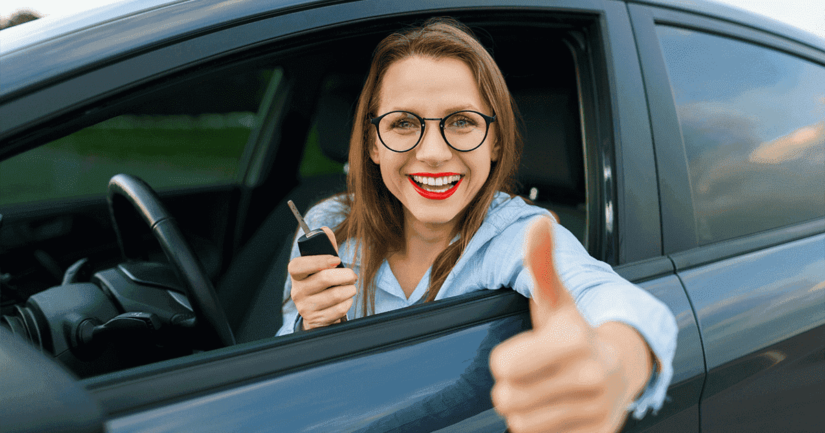 Imagem de uma mulher dentro do carro em uma das mãos segurando a chave e na outra fazendo apontando o polegar para cima.